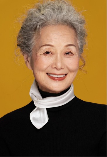 Silver-haired woman against a yellow background, interview portrait reference